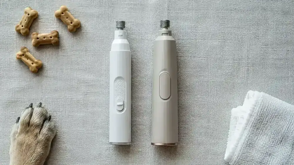 Two dog nail grinders placed side by side on a wooden surface next to a dog paw